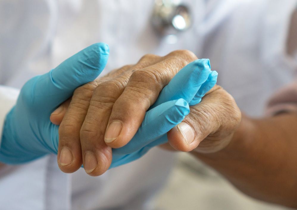 A doctor wearing gloves holds a patient's hand.