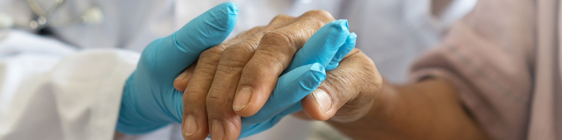 A doctor wearing gloves holds a patient's hand.